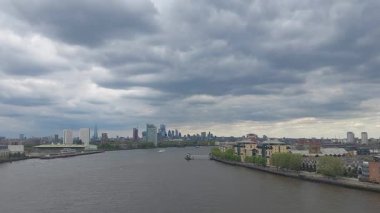 Modern bir şehir manzarası üzerinde dramatik bulutlar beliriyor, çağdaş binalarla dolu geniş bir nehir manzarası, kentsel sükunet ve mimari yenilikleri yakalıyor.