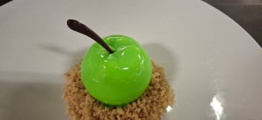 Gerçekçi yeşil elma şekilli bir tatlıyı tabakta parçalanmış bir tabakta sunan gastronomik bir sunum. Mutfak tasarımları, güzel yemekler ve yenilikçi tatlı sanatları için ideal..