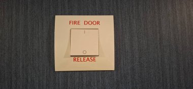 Kamu veya özel tesislerdeki yangın güvenlik mekanizmalarını vurgulayan, mavi desenli bir duvara monte edilmiş bir yangın kapısı açma düğmesinin yakın çekimi.