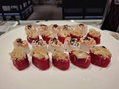 Beyaz bir tabakta zarif bir şekilde servis edilen eşsiz malzemeler ve renkli sunumlar içeren güzel düzenlenmiş bir suşi seçimi..