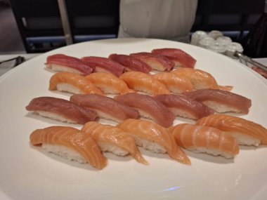 Beyaz bir tabakta sunulan somon ve tuna nigiri çeşitlerinin sunduğu iştah açıcı taze suşi çeşitleri Japon mutfağının sanatını, canlı renklerini ve gurme deneyimi için hassas hazırlıkları vurguluyor..