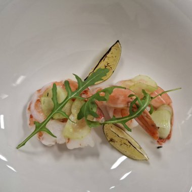 Taze karidesler, salatalık dilimleri, roka ve kavrulmuş limon dilimlerini beyaz bir tabakta ustalıkla hazırlanmış gurme mutfağı ve rafine yemek sunumunu vurgulayan aperatifler..