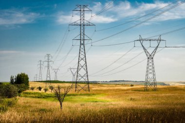 Powerlines hanging from tall steel towers overlooking natural grasslands and prairie landscape in rural Alberta near Calgary. clipart