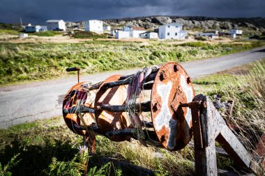 Keels Newfoundland Kanada 'daki küçük ahşap evlere bakan uzun çimenlerde uzanan ticari bir balıkçı teknesinin makarası Discovery Trail manzaralı güzergahı boyunca.