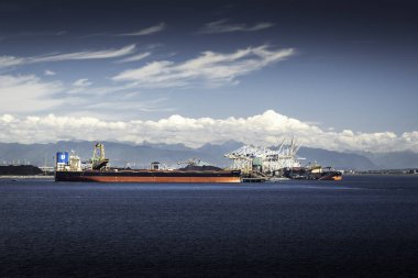 Roberts Bank British Columbia Canada, 24 Temmuz 2023: Bir yük gemisi, arka planda Vancouver şehriyle birlikte Kanada Rocky Dağları 'ndan çıkarılan kömür madenleriyle dolu..
