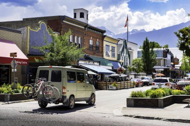 Revelstoke British Columbia, 9 Temmuz 2023: Dağ bisikletli bir karavan, arka planda Selkirk Dağları 'nın bulunduğu miras binalarının altındaki yerel işletmelere bakarak ana caddede ilerliyor..