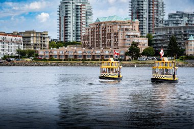 Victoria British Columbia Kanada, 12 Temmuz 2023: Bir çift su taksi botu şehir merkezindeki apartman binalarının dar geçitlerinden geçiyor.