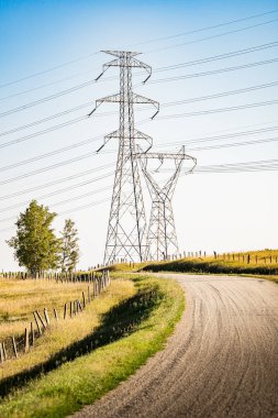 Rocky View County Kanada 'sındaki Alberta bozkırlarına bakan çakıllı yolun yanında elektrik hatları olan iletim kuleleri..