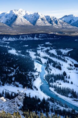 Tünel Dağı 'ndan alınan Banff Ulusal Parkı' ndaki karla kaplı dağların arasından akan kış nehrine bakıyorum..