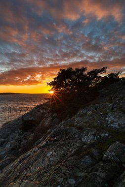 Parlak günbatımı, dramatik gökyüzü ve huzur dolu kayalar ve deniz ufkuyla nefes kesici bir sahil sahnesi. Huzurlu ortamda doğa güzelliği parıldıyor..