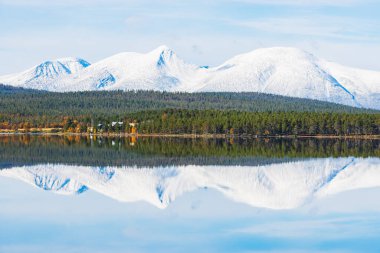 Karlı dağ ve durgun bir göle yansıyan yeşil orman.