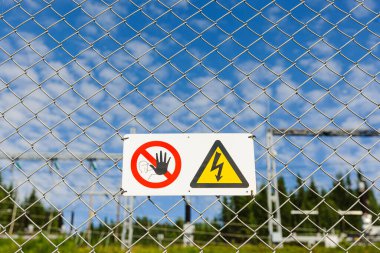 Warning sign on fence in front of high voltage transformer substation clipart