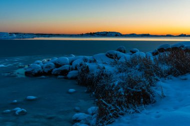 Şok edici bir kış günbatımı İsveç 'te sakin, donmuş denizi ve karla kaplı toprakları aydınlatır..