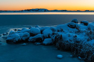 Şok edici bir kış günbatımı İsveç 'te sakin, donmuş denizi ve karla kaplı toprakları aydınlatır..