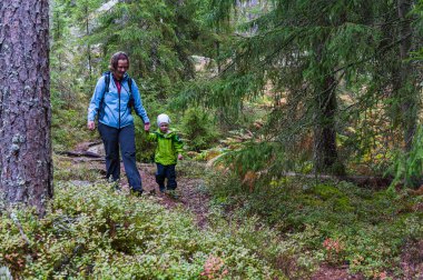 Genç bir çocuk ve annesi yemyeşil ağaçlar ve bol bitki yetiştirme ile çevrili vahşi doğada sakin bir yürüyüş yapıyorlar..