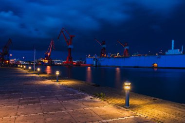 Alacakaranlıkta vinç ve rıhtımla aydınlatılmış tersane.