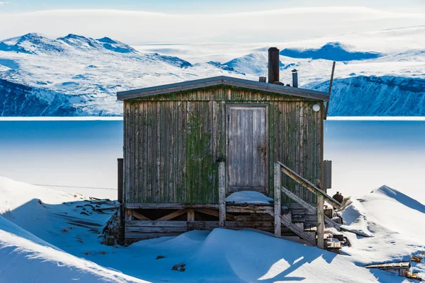 A wooden cabin in a snowy mountain landscape in Greenland.