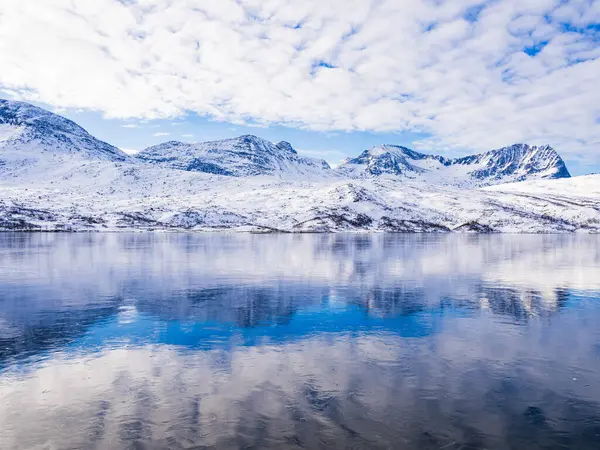 Snowy mountain reflected in a tranquil frozen lake in Norway