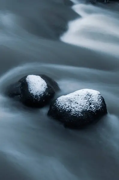 Icy river with flowing water and snowy rocks in winter.