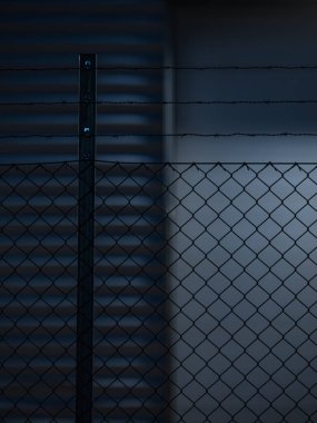 Bu görüntü zincirli tel örgülerin bir kısmını yakalıyor ve kıvrımlı metal bir duvarın üzerine belirgin bir gölge düşüyor. Işık ve gölge arasındaki zıtlık, ışık açılarının düşük olduğu akşam çekildiğini gösteriyor..