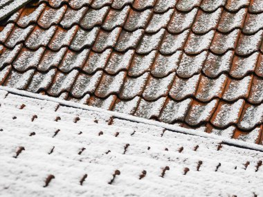 Göteborg 'un çatıları, terakotta fayanslarını kaplayan taze bir kar tabakası gibi parlayarak beyaz tozuyla tam bir zıtlık yaratıyor. Kar taneleri de ön plandaki ahşap yüzeye hafifçe yerleşmiş. Bu da son kar yağışını gösteriyor. 