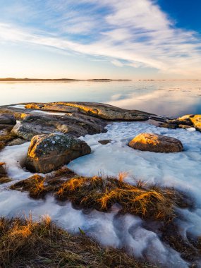İsveç 'teki Sillvik' te kayalık kıyı şeridinin kısmen buz ve karla kaplı olduğu yerde, huzurlu bir kış manzarası güneşin batışını yakalar. Sakin deniz gökyüzünün pastel renklerini yansıtarak doğal manzaranın sükunetini arttırır..