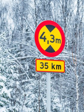 A street sign mounted on a metal pole stands tall amidst a blanket of snow on a winter day. The sign indicates a restricted vehicle height, warning drivers of potential obstructions. The white snow contrasts with the red and white sign, creating a st clipart