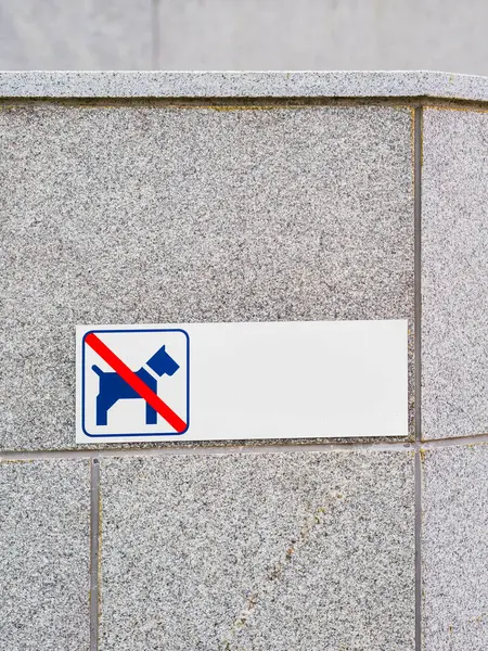 This sign, attached to a gray stone wall in Sweden, clearly indicates that the area is off-limits for dog walking or resting. The blue and white sign features the universally recognized symbol of a dog within a red circle and a diagonal line indicati
