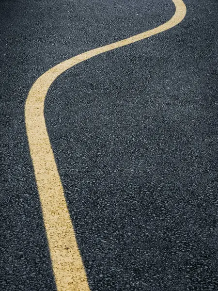 A road in Sweden with a vibrant yellow curved line painted down the center, guiding vehicles along the smooth pavement.