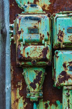 A close-up image showcasing three rusty green electrical boxes mounted on a weathered wall. The boxes exhibit signs of significant wear and tear, with peeling paint and rust visible across their surfaces. The wall itself appears to be made of wood an clipart