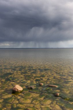 Vanern Gölü 'nün üzerinde kara bulutlar belirir, sakin sulara ve kayalık kıyılara gölgeler bırakır. Atmosfer yaklaşan bir fırtınayı gösteriyor, dingin güzelliği arttırıyor..