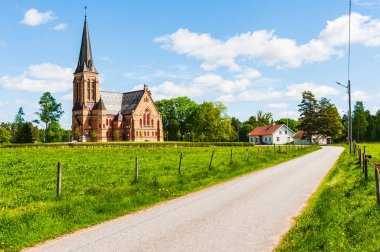 İsveç kırsalında sakin bir yol esiyor, güzel tasarlanmış bir kiliseye doğru, yemyeşil ve antika evlerin arasına kurulmuş, hepsi de parlak güneş ışığıyla yıkanmış..