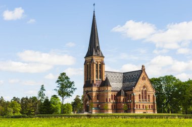Büyüleyici kilise, canlı yeşil ağaçlara karşı sergilenen muhteşem tuğla mimarisini sergiliyor. Güneş ışığı sahneyi aydınlatır, dingin güzelliğini arttırır..