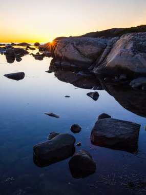 Güneş İsveç kıyılarında batarken, gökyüzü ılık renklerle parlarken ışık pürüzsüz sularda ve pürüzsüz kayalarda dans ediyor ve sakin bir atmosfer yaratıyor..