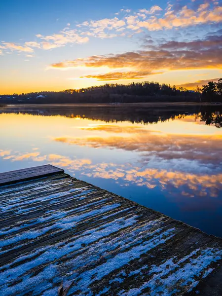 Renkli günbatımı, dingin bir göl boyunca ılık renkler bırakır ve suya çarpıcı yansımalar yaratır. Kırsal ahşap rıhtım doğal güzelliği artırmak için olay yerine sınır çiziyor..