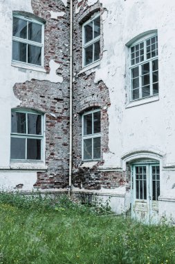 Eski bir sanatoryumun çürüyen duvarları, doğa tarafından geri alınırken ihmal belirtileri gösteriyor. Çatlak tuğla ve soyulan boya binanın geçmişini ve terk edilişini vurguluyor..