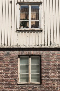 Two sets of windows on a weathered building in Gothenburg showcase the unique architectural style. The upper window is framed by wooden panels, while the lower window features a brick surround. clipart