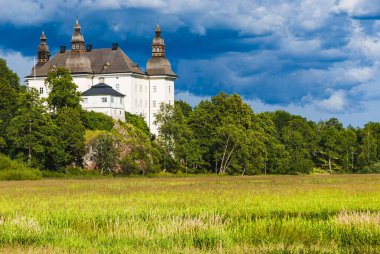 Ekenas Castle stands majestically amidst a vibrant landscape of green fields and trees, with striking clouds forming an impressive backdrop, showcasing the beauty of Swedish architecture. clipart