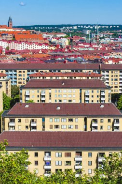 Göteborg kentsel peyzajında, İsveç mimari tarzını yansıtan, tepe ve mavi gökyüzünün zeminine kurulmuş sarı cepheli ve kırmızı çatılı konut binaları yer almaktadır..