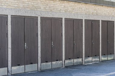 Several garages stand in a neat row, each featuring a simple brown door. The clean lines and muted colors reflect a minimalist style typical of urban areas in Gothenburg, Sweden. clipart