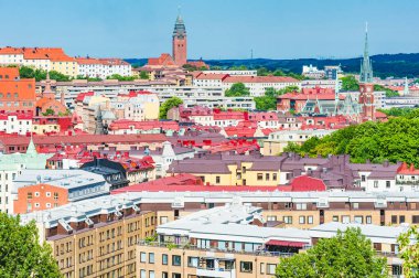 Parlak renkli çatılar Göteborg 'da canlı bir siluet oluşturur. Sahnede açık mavi gökyüzü altında tarihi mimari ve modern binaların bir karışımı sergileniyor..