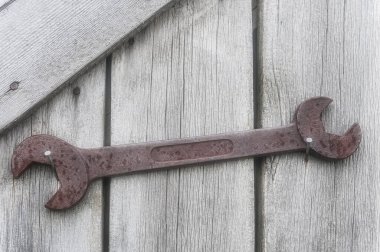 Büyük, paslı bir İngiliz anahtarı İzlanda 'da yıpranmış ahşap bir duvara sıkıca bağlanmış. Kırsal bir ortamda insan yapımı aletlerle doğanın karışımını vurguluyor..