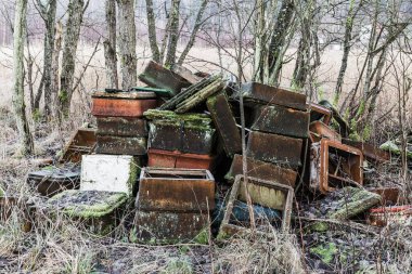 İsveç 'in ormanlık bir bölgesindeki ağaçlar arasında yıpranmış konteynır ve kalıntılardan oluşan bir küme görülebilir. Paslı metali yosun kaplıyor, sahnenin terk edilmiş görüntüsünü vurguluyor..