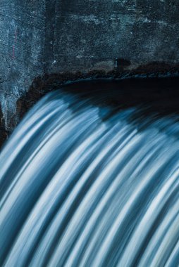 Su, beton bir yapının üzerinden zarif bir şekilde akar ve sakin bir öğleden sonra İsveç 'te sakin bir manzara yaratır. Dalgalanan etkiler doğanın güzelliğini ve sükunetini vurgular..