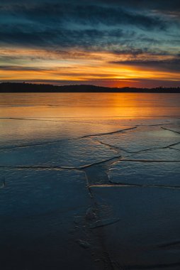 Günbatımı İsveç 'te donmuş bir göl boyunca parlak renkler sergiliyor. Güneş ışığı söndükçe gökyüzü maviden turuncuya dönüşüyor ve yüzeydeki karmaşık buz kalıplarını vurguluyor..