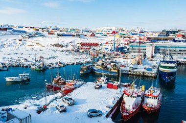 Ilulissat Limanı 'nda renkli kasaba ve karla kaplı araziyle çevrili buzun üzerinde dinlenen tekneler yer alıyor. Parlak gökyüzü bu Grönland limanının canlı atmosferine ekleniyor..