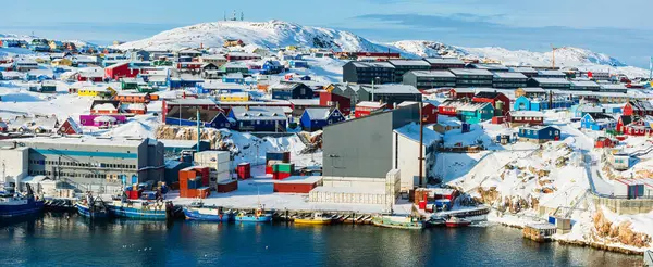 Canlı, renkli evler Grönland 'daki Ilulissat limanı boyunca uzanan karlı arazide berrak gökyüzünün altındaki buzlu arazide canlı bir yerleşim gösteriyor..