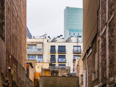 Barcelona 'daki dar sokak manzarası bulutlu gökyüzünün altında modern mimarinin yanında tarihi binaların yan yana dizilişini sergiliyor..