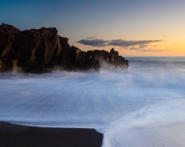 Güneş batarken dalgalar Madeira 'nın engebeli kayalarına çarpar. Yumuşak renkler ve yumuşak hareketlerle dolu kıyı şeridinin çarpıcı bir görüntüsünü yaratır..