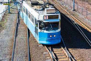 Tramvaylar canlı bahar sezonunda Göteborg 'da sorunsuz bir şekilde çalışarak, kentteki canlı atmosferi ve kentsel hareketliliği vurguluyor. Yolcular manzaralı yolculuğun tadını çıkarıyorlar..
